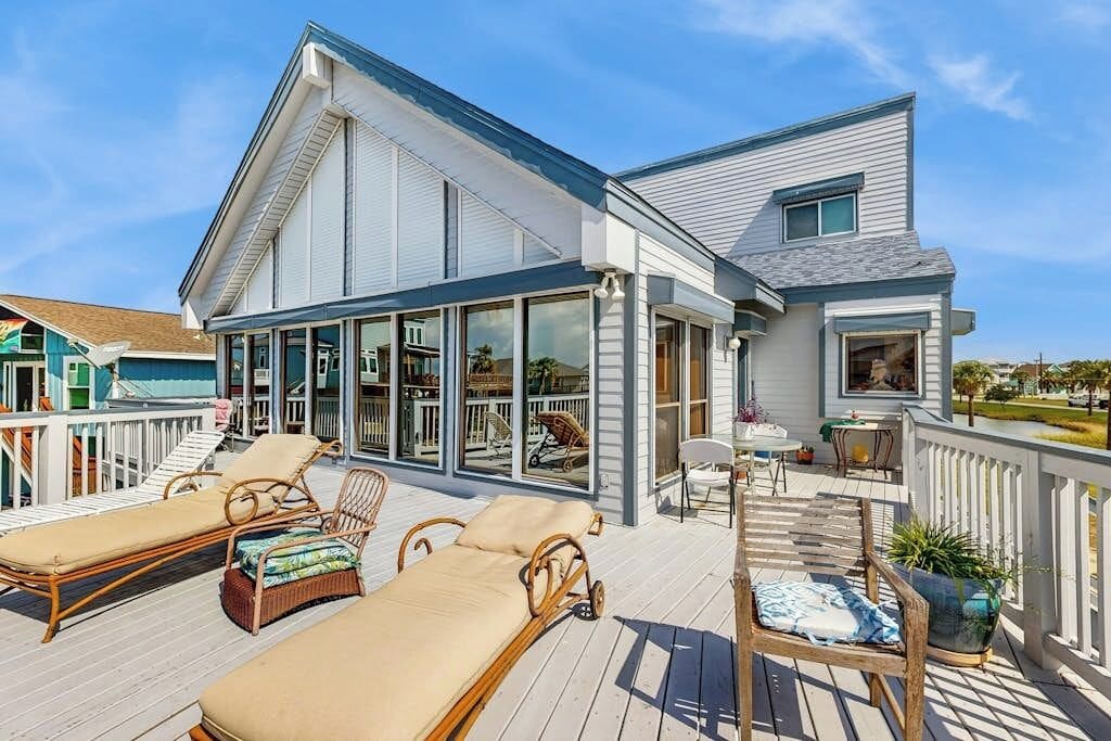 A house with a large deck, multiple lounge chairs, and a covered outdoor area.