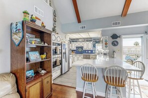 A kitchen with a central island, white bar stools, and a wooden cabinet with decorative items. - Tiki Hideaway - Canal-Front, Big Deck & Dogs OK (Tiki Island)
