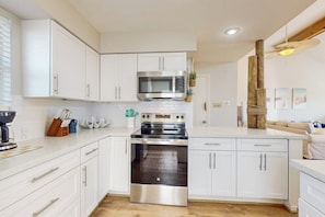 A modern kitchen with white cabinets, stainless steel appliances, and a wooden floor. - Ocean Breeze Getaway (Galveston)