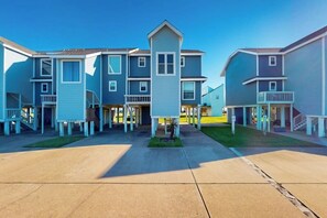 A row of townhouses with a central entrance, each with a balcony and a small front yard. - Ocean Breeze Getaway (Galveston)
