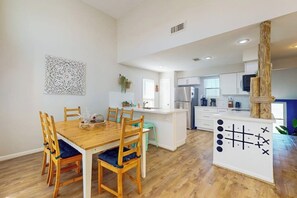 A modern kitchen with white cabinetry, a central island, and a dining area with wooden chairs and a table. - Ocean Breeze Getaway (Galveston)