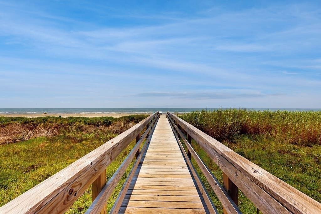 A wooden boardwalk leading to a beach with a clear sky.
