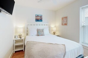 A bedroom with a bed, bedside tables, lamps, and artwork on the walls. - Mapacebo - Pool & Walk to Beach (Port Aransas)