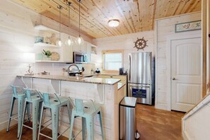 A kitchen with a central island, bar stools, a stainless steel refrigerator, and a wooden ceiling. - Mapacebo - Pool & Walk to Beach (Port Aransas)