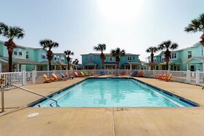 A swimming pool with lounge chairs and palm trees, surrounded by buildings with a light blue facade. - Mapacebo - Pool & Walk to Beach (Port Aransas)