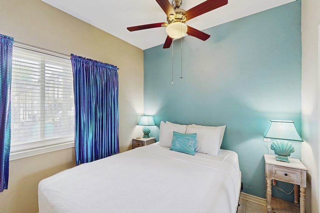 A bedroom with a bed, two bedside tables, a ceiling fan, and curtains.