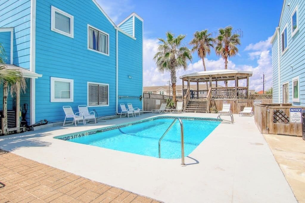 Un bâtiment bleu avec une piscine, des chaises longues et un kiosque.