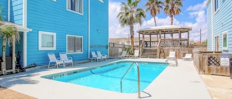 Un bâtiment bleu avec une piscine, des chaises longues et un kiosque.