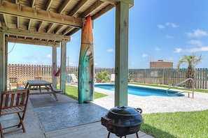 An outdoor patio with a barbecue grill, pool, and wooden deck furniture. - Gulf Breezes Entire Home (Port Aransas)