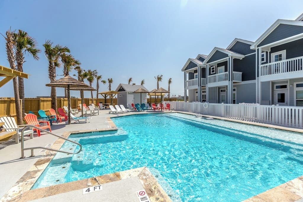A swimming pool with lounge chairs and umbrellas, surrounded by buildings with balconies.
