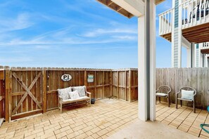 A covered patio area with a wooden fence, a bench, and two chairs. - Tiki House - Ocean Views, Pool, Steps to Beach (Corpus Christi)