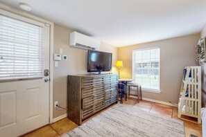 Ein Zimmer mit Fernseher auf einer Holzkommode, einer Lampe und einem weißen Stuhl.
