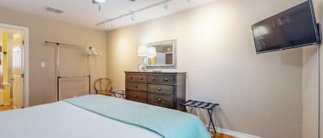 Un dormitorio con una cama, un aparador, un espejo, un ventilador de techo y un televisor montado en la pared.