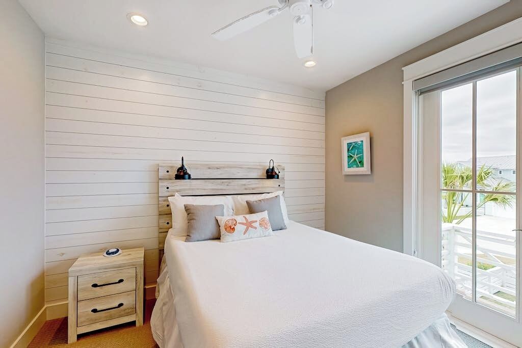 A bedroom with a bed, a nightstand, a ceiling fan, and a window with a view.