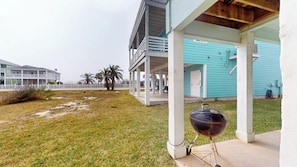 A covered outdoor area with a grill, a white fence, and a turquoise building in the background. - Bella Vista #25 - Water Views, Pool & Hot Tub (Port Aransas)