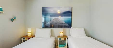 Habitación de hotel con dos camas, una mesita de noche con lámpara, un cuadro colgado en la pared y un pequeño adorno azul turquesa en el suelo.