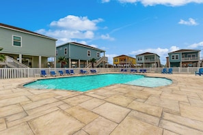 A swimming pool with a white fence and blue lounge chairs, surrounded by colorful houses. - Blue Diamond Cottage (Rockport)