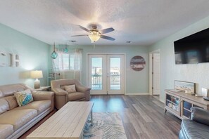A living room with a ceiling fan, a sofa, a coffee table, and a TV on a stand. - The Seashell Getaway (Rockport)