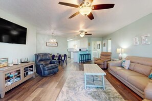 A living room with a ceiling fan, a sofa, a coffee table, and a TV on the wall. - The Seashell Getaway (Rockport)