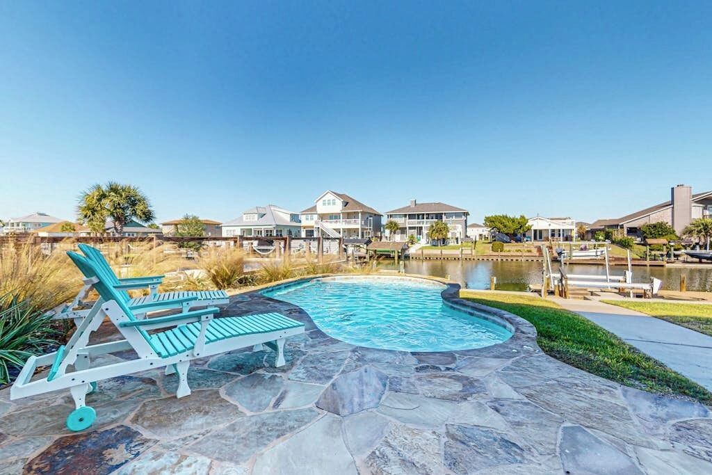 Ein Swimmingpool mit Liegestühlen, einer Steinterrasse und Blick auf Häuser im Hintergrund.