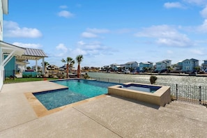 A swimming pool with a view of a river and houses in the background. - Tortuga Palms - Bayfront, Heated Pool & Hot Tub (Rockport)
