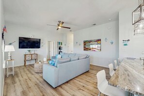 A modern living room with a light blue sofa, a dining table with chairs, a ceiling fan, and a flat-screen TV. - Paradise on the Coast (Rockport)