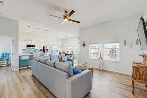 A spacious living area with a large gray sofa, a ceiling fan, and a kitchen in the background. - Paradise on the Coast (Rockport)