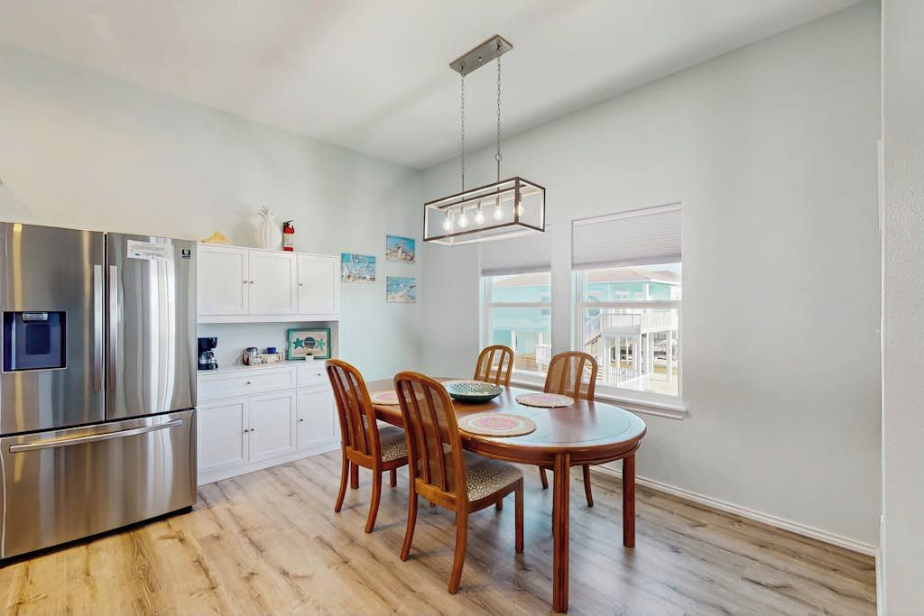 Een moderne keuken met een roestvrijstalen koelkast, een houten eettafel met stoelen en een hanglamp.