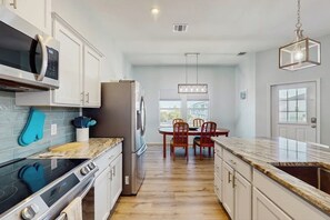 A modern kitchen with a built-in oven, microwave, and refrigerator. There is a dining area with a table and chairs. - Paradise on the Coast (Rockport)