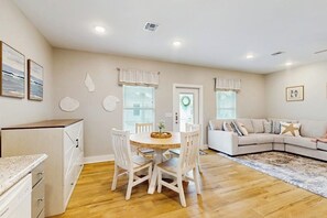Ein Wohnzimmer mit rundem Tisch und Stühlen, einer Couch und einer Küchenzeile mit Schränken und Arbeitsplatte.