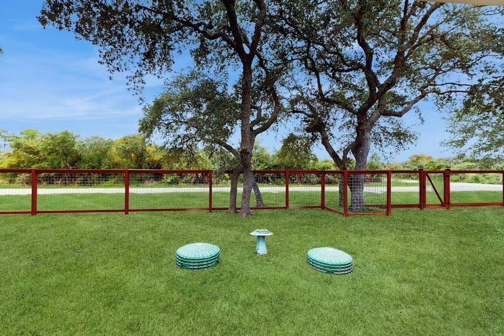 Un espacio exterior cercado con un árbol, una pequeña mesa y dos taburetes redondos.