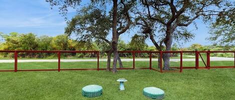 Un espacio exterior cercado con un árbol, una pequeña mesa y dos taburetes redondos.