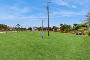 A grassy field with a utility pole, a blue electrical box, and a red fence. - Packsaddle Beach House (Rockport)