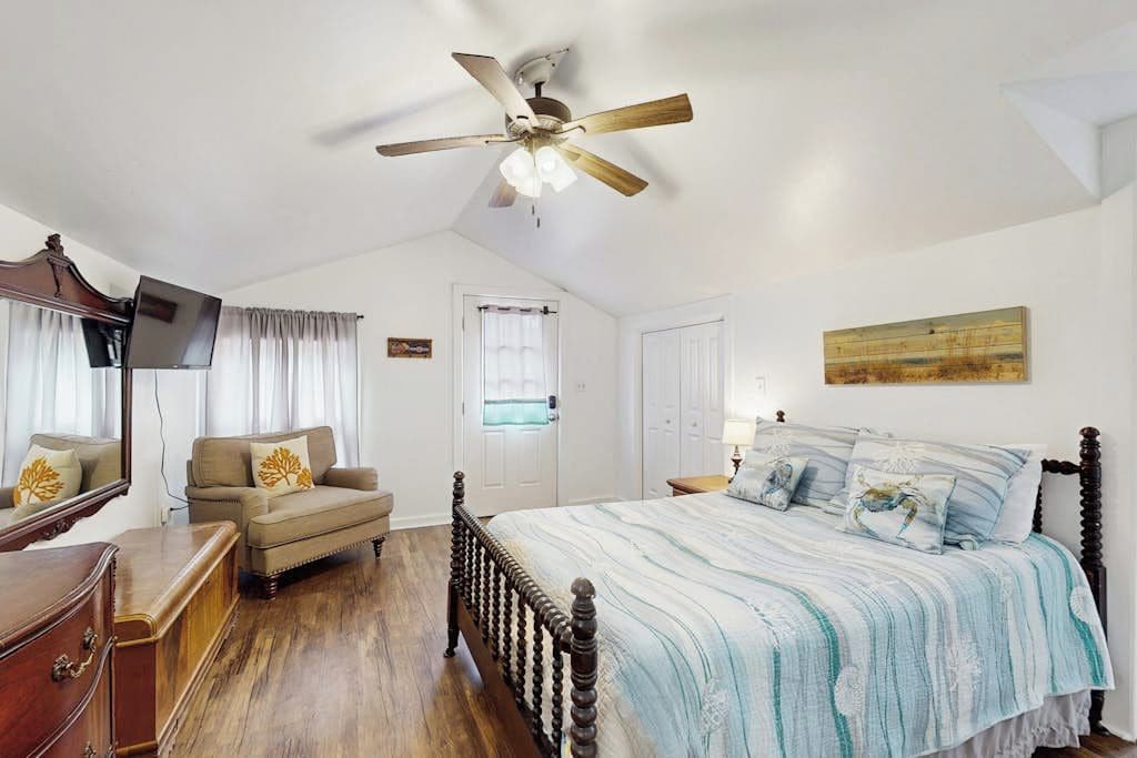 Un dormitorio con cama, ventilador de techo, cómoda, televisor y una puerta.