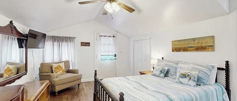 A bedroom with a bed, a ceiling fan, a dresser, a television, and a door.
