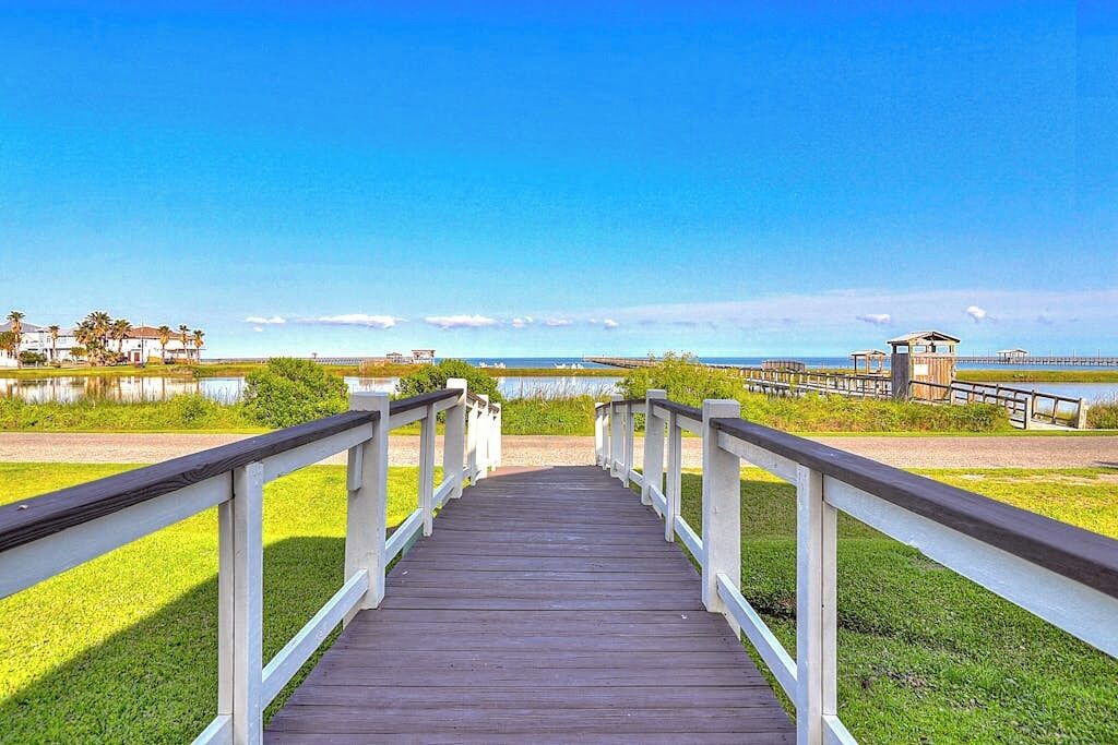 Ein Holzsteg führt zu einem Strand unter blauem Himmel.