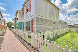 Un bâtiment à deux étages, à l’extérieur blanc et aux volets rouges, avec une clôture en piquets blancs et un chemin pavé.