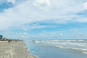 Ein Strand mit einem Leuchtturm, sandigem Ufer und Wellen.