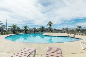 A swimming pool with lounge chairs and palm trees. - Las Palmas Retreat - Gulf Views & Community Pool (Galveston)