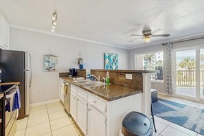 A modern kitchen with a granite countertop, white cabinets, a built-in oven, and a ceiling fan. - Maravilla Condos - Anchors Away (Galveston)