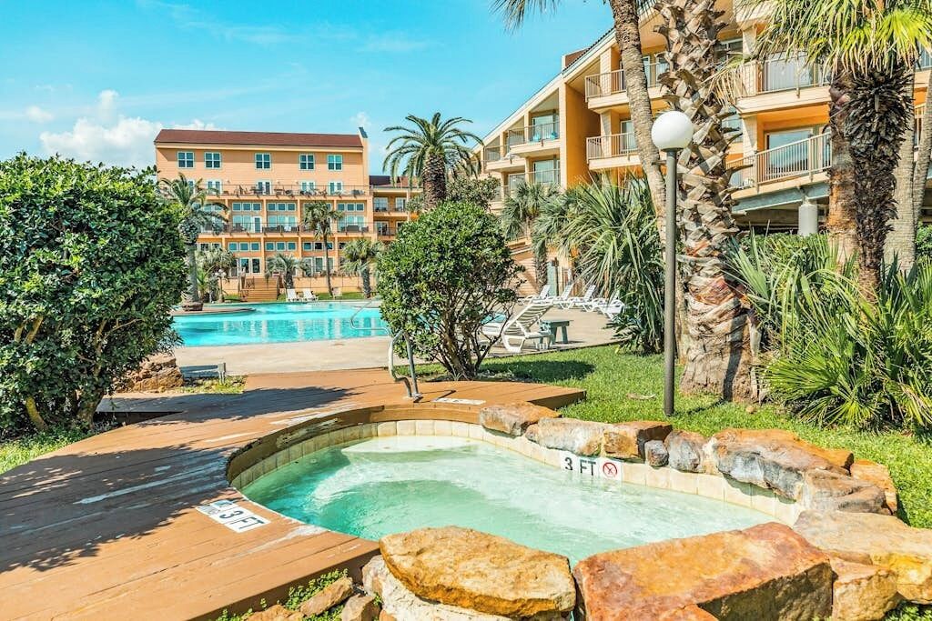 Un hôtel doté d’un espace piscine comprenant un jacuzzi et une piscine classique, le tout entouré de verdure et de palmiers.