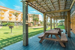 Un espace extérieur abrité avec des tables de pique-nique, une pelouse et un bâtiment en arrière-plan.