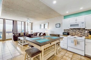 A modern kitchen with white cabinets, a microwave, and a stove. There is a dining area with a table and chairs. - Fairway Villa #204 - 2 Balconies, Pool & Hot Tub (Corpus Christi)