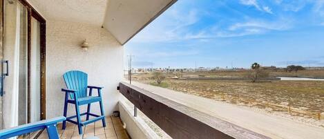 A balcony with a view of a flat landscape, a chair, and a table.