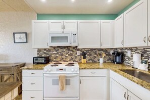 A kitchen with white cabinets, a microwave, a stove, and a tiled backsplash. - Fairway Villa #204 - 2 Balconies, Pool & Hot Tub (Corpus Christi)