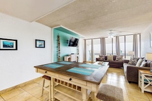 A living room with a wooden dining table, a sofa, and a television. - Fairway Villa #204 - 2 Balconies, Pool & Hot Tub (Corpus Christi)