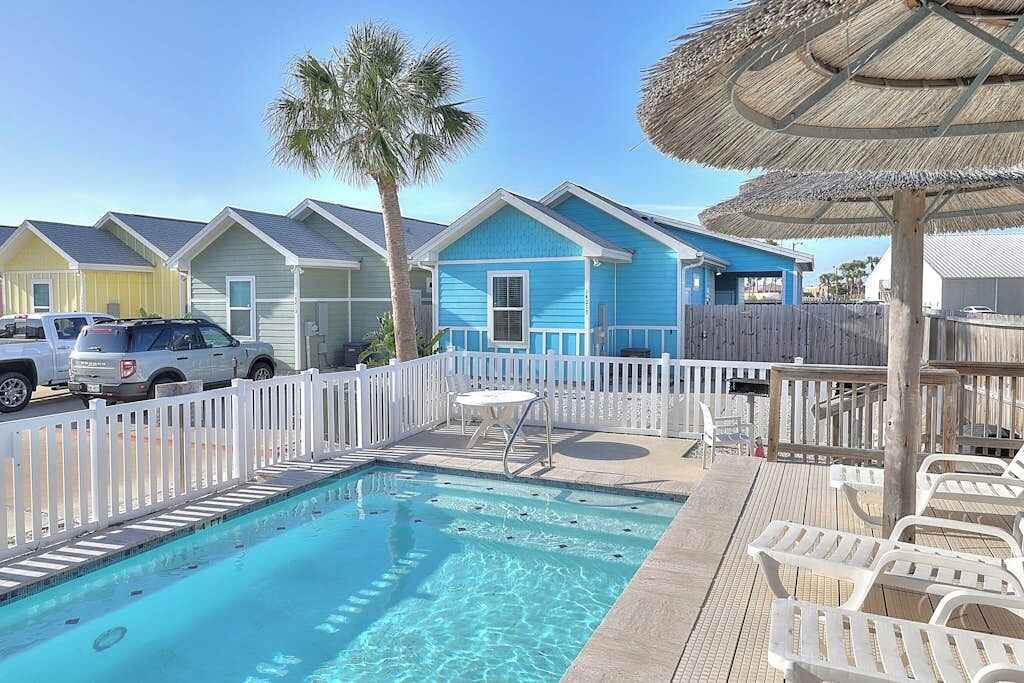 A pool area with a clear blue pool, white lounge chairs, and a thatched umbrella.