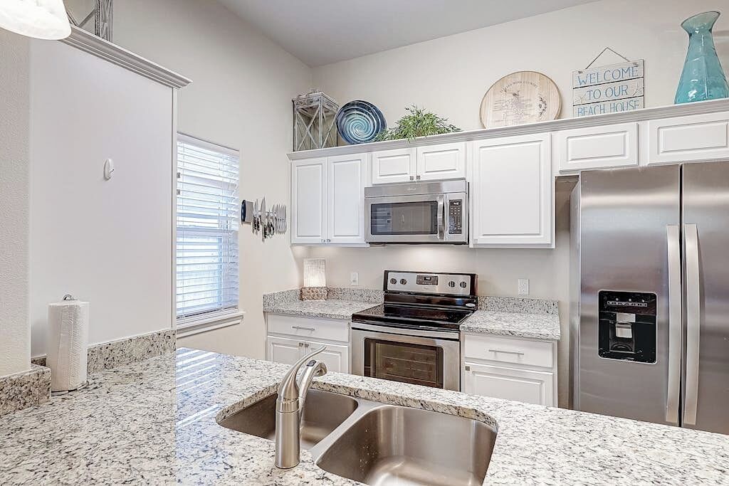 Una cocina con gabinetes blancos, un refrigerador de acero inoxidable, un microondas, un horno y una encimera de granito.
