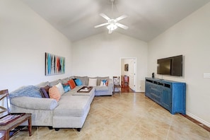A spacious living room with a grey sectional sofa, a flat-screen TV mounted on the wall, and a ceiling fan. - Anegada Village - Love & Luck (Corpus Christi)