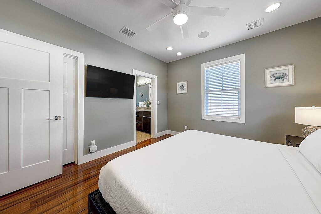 A bedroom with a bed, a ceiling fan, a window with blinds, and a door leading to a bathroom.